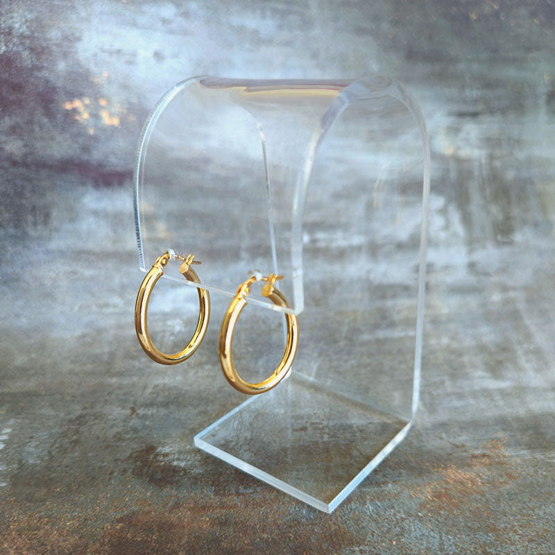 Gold hoop earrings on a clear stand against a textured gray background