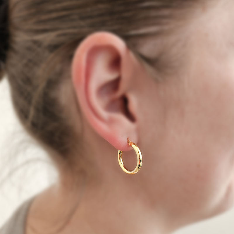 Close-up of a person wearing a gold hoop earring with a blurred background