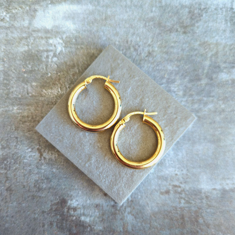 Gold hoop earrings on a gray stone surface