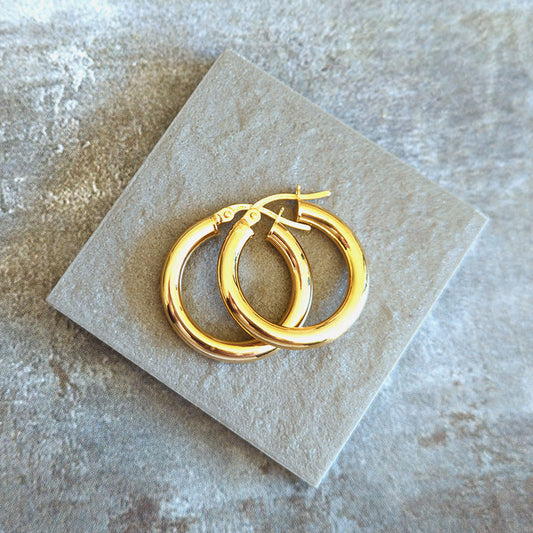 Gold hoop earrings on a textured stone surface