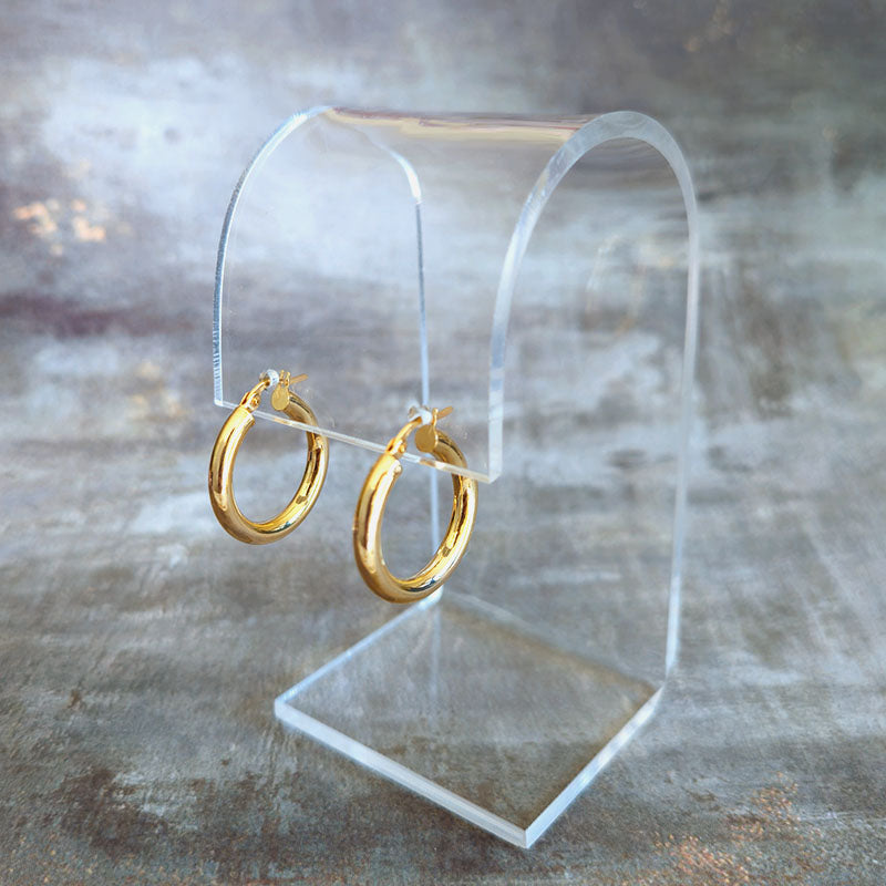 Gold hoop earrings on a clear stand against a textured gray background