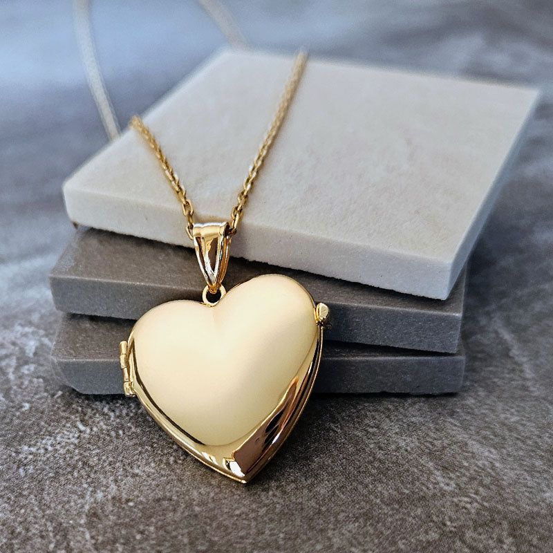 Gold heart-shaped locket on a chain against a neutral background