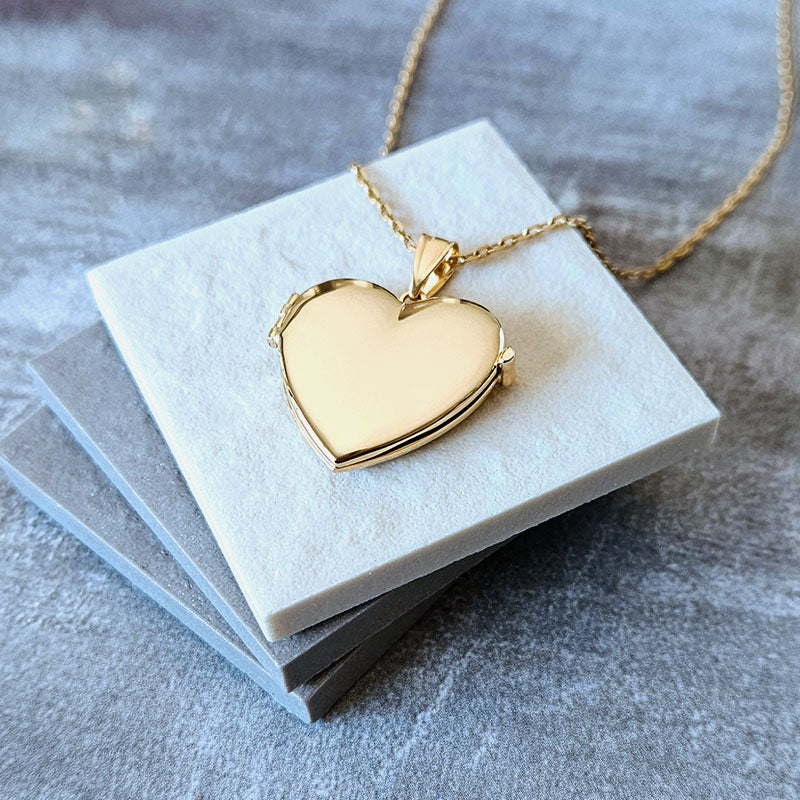 Gold heart-shaped locket on a white card with a gray background