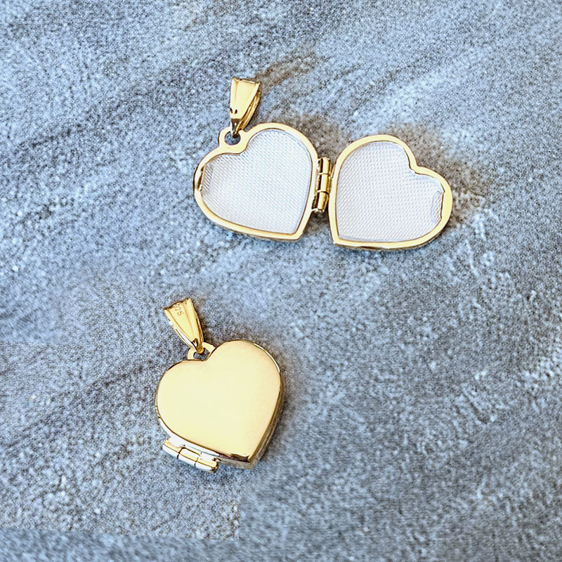 Two gold heart-shaped locket pendants on a textured gray surface