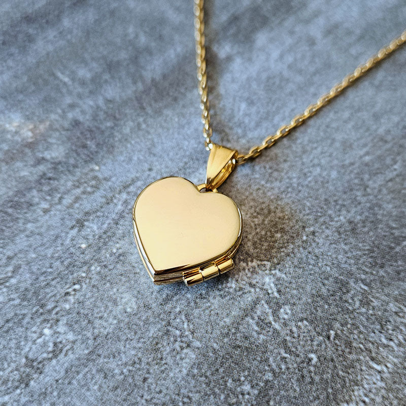 Gold heart-shaped locket on a chain against a textured gray background