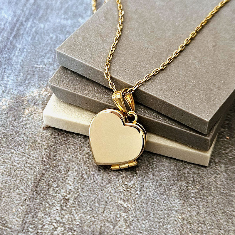 Gold heart-shaped locket necklace on a textured surface