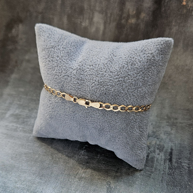 Gold chain bracelet on a gray textured pillow against a dark background