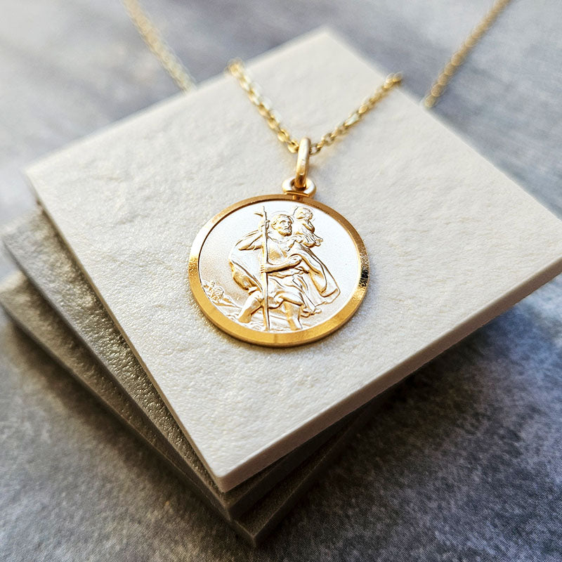 Gold necklace with a circular St Christopher pendant on a textured surface