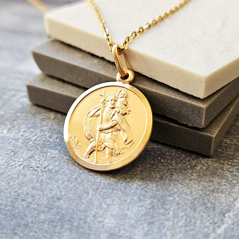 Gold St Christopher pendant necklace on a textured surface