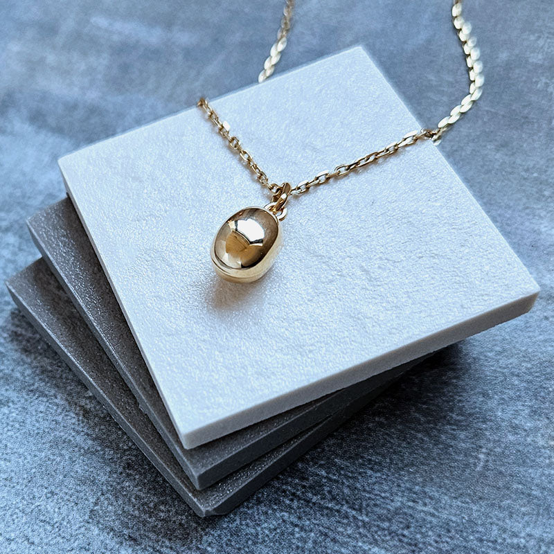 Gold necklace with an oval pendant on a gray stone surface