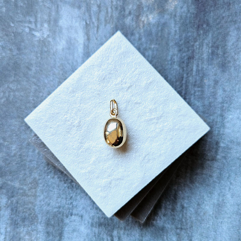 Gold pendant on a white square card with a gray textured background