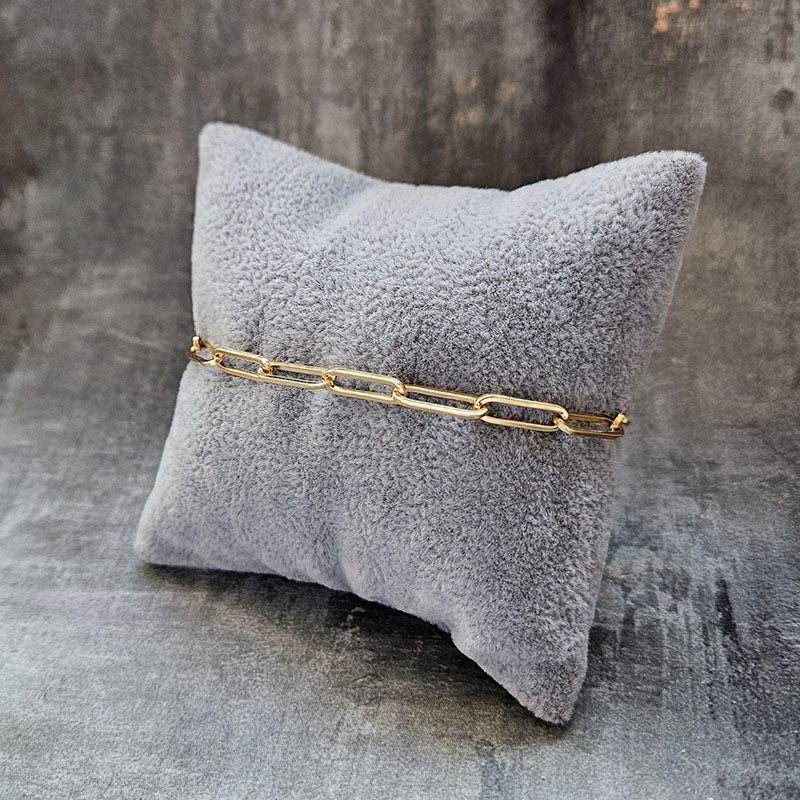 Gold chain bracelet on a gray textured pillow against a gray background