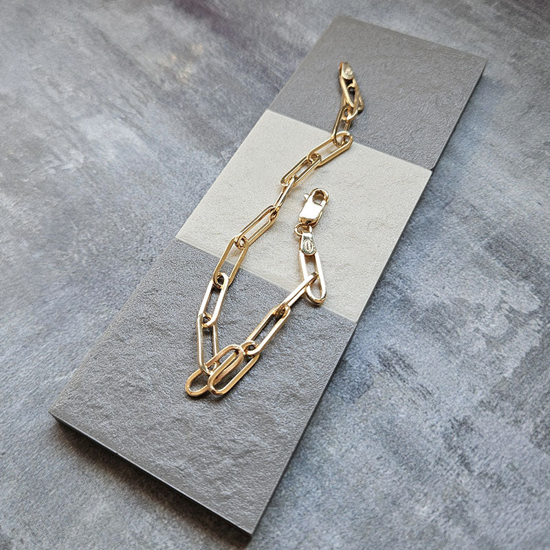 Gold paperclip bracelet on a gray card with a gray background