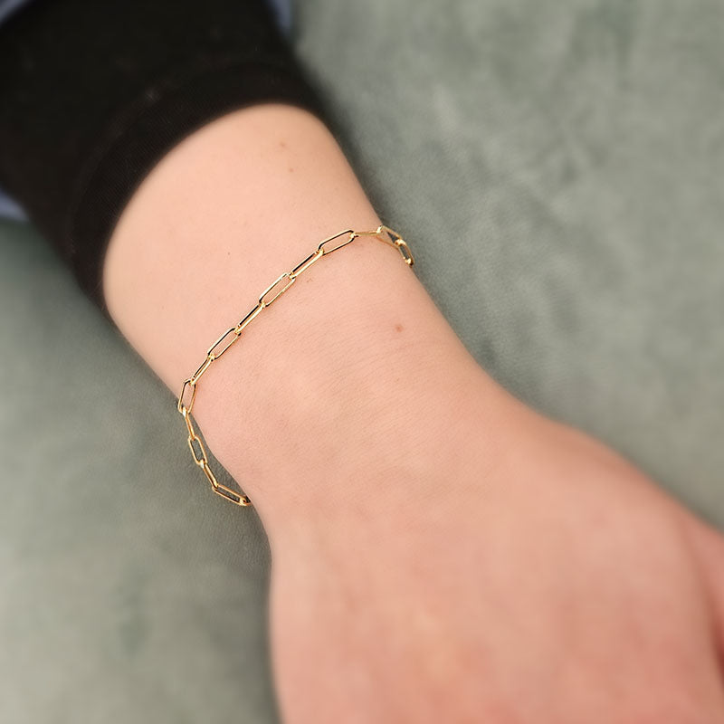 Gold chain bracelet on a wrist against a neutral background