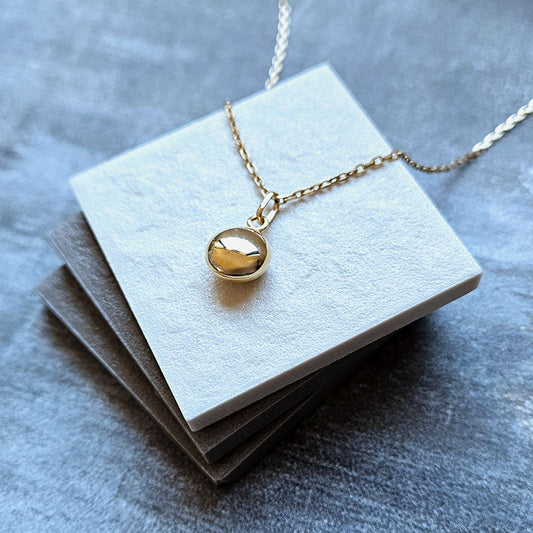 Gold necklace with a round pendant on a gray surface