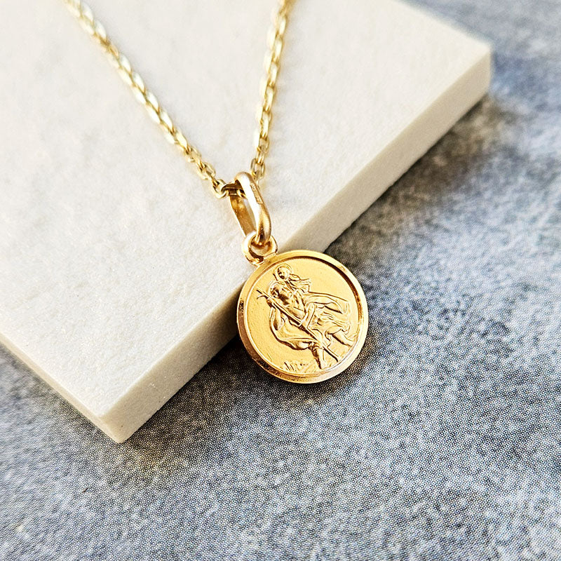 Gold necklace with a round St Christopher pendant on a textured surface