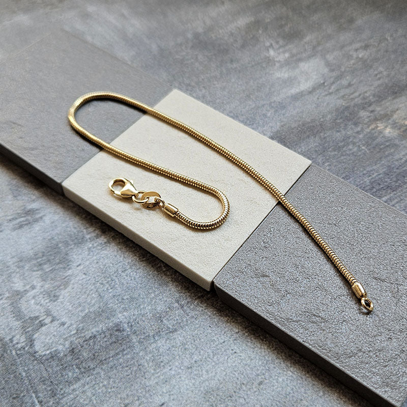 Gold snake bracelet on a gray stone surface