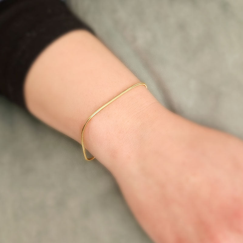 Gold bracelet on a wrist with a neutral background