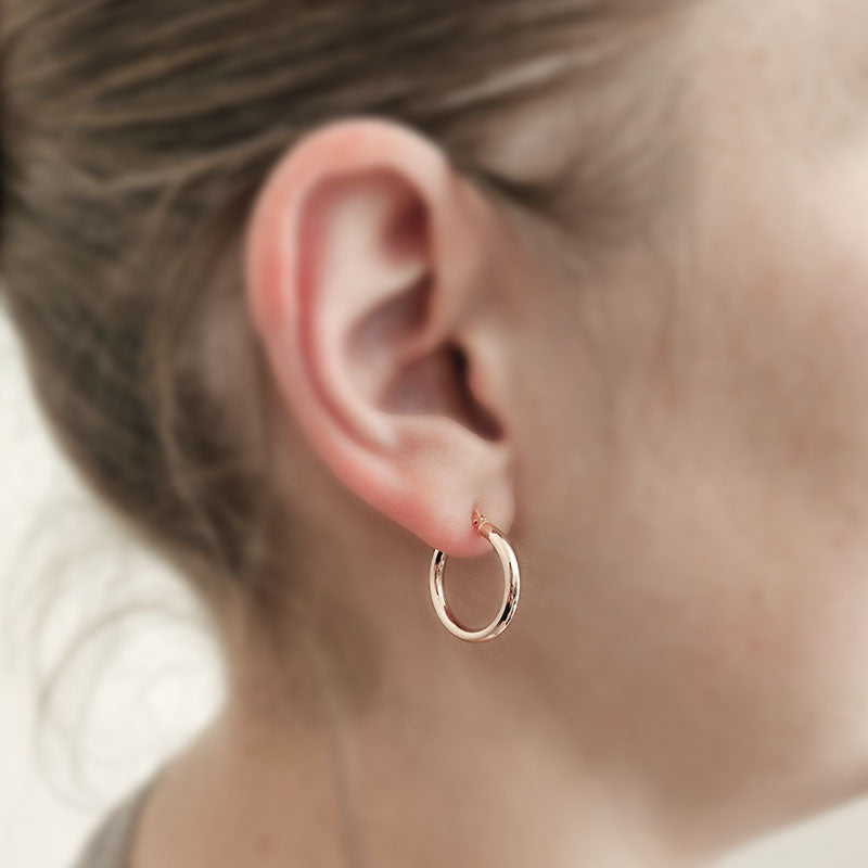 Rose gold hoop earring worn by a person with blurred background