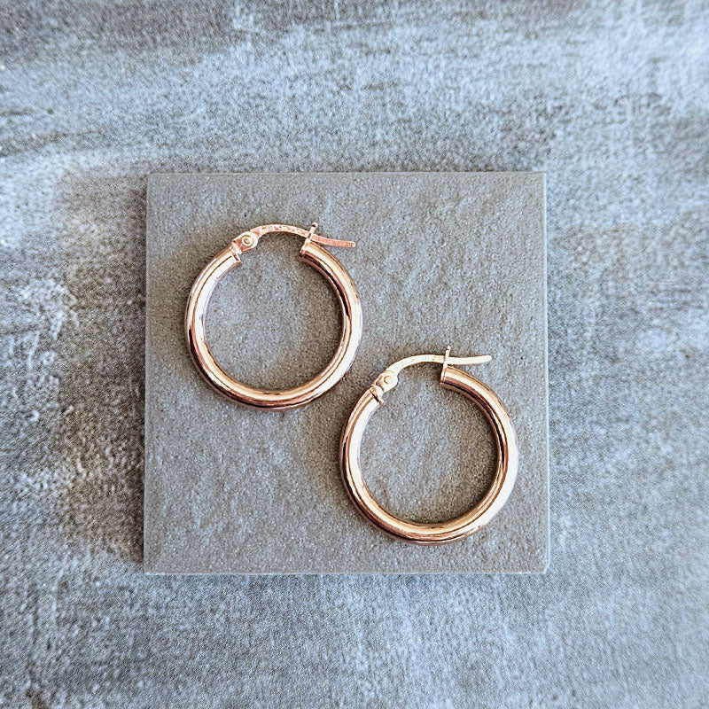 Rose gold hoop earrings on a textured stone surface