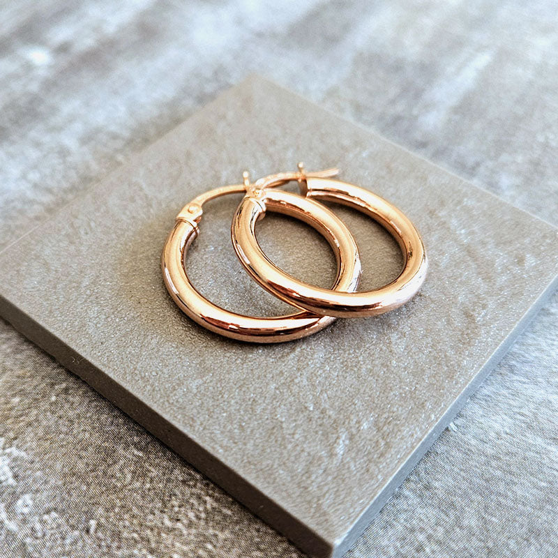 Rose gold hoop earrings on a stone surface