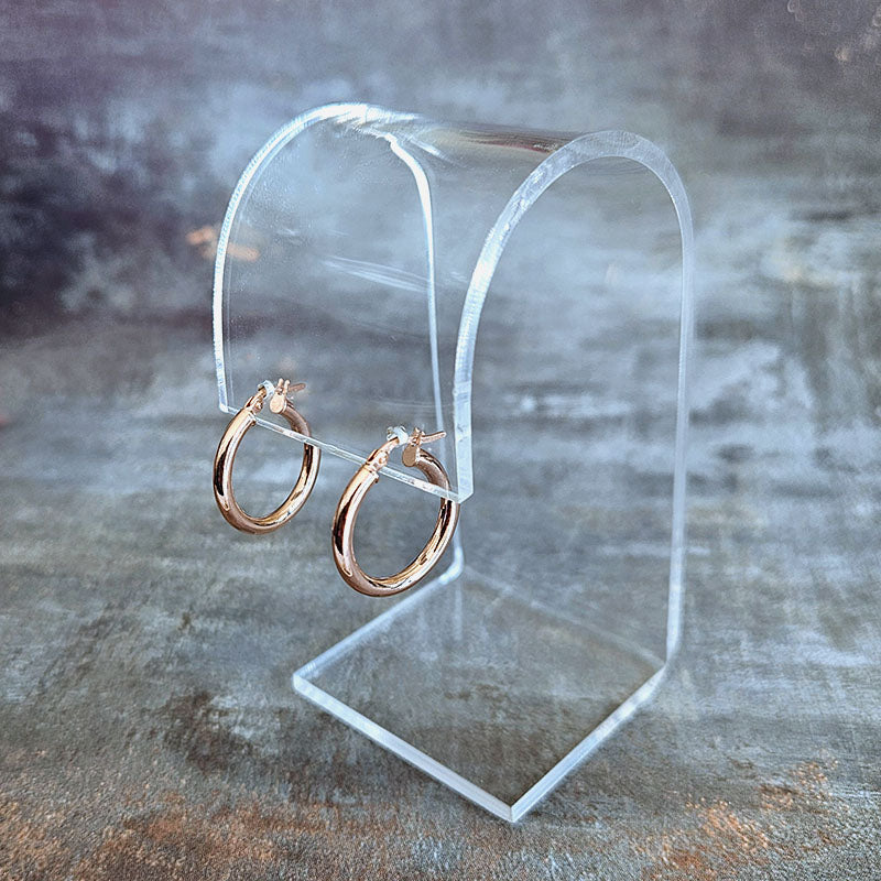 Rose gold hoop earrings on a clear stand against a textured gray background