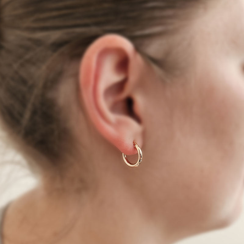 Close-up of a person wearing a gold hoop earring with a blurred background