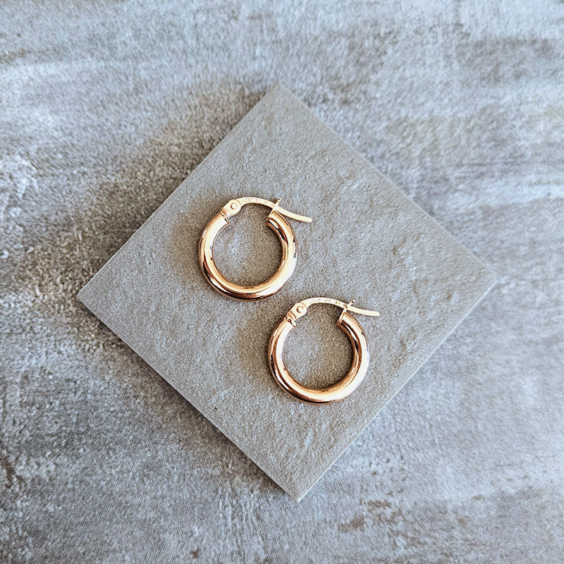 Rose gold hoop earrings on a stone surface