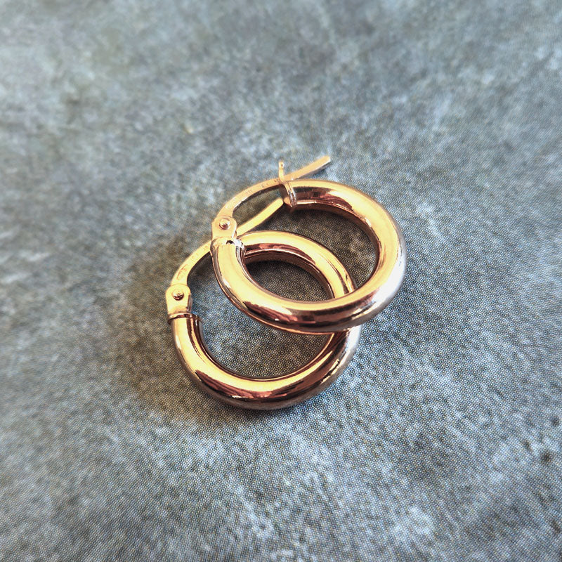 Rose gold hoop earrings on a textured gray surface