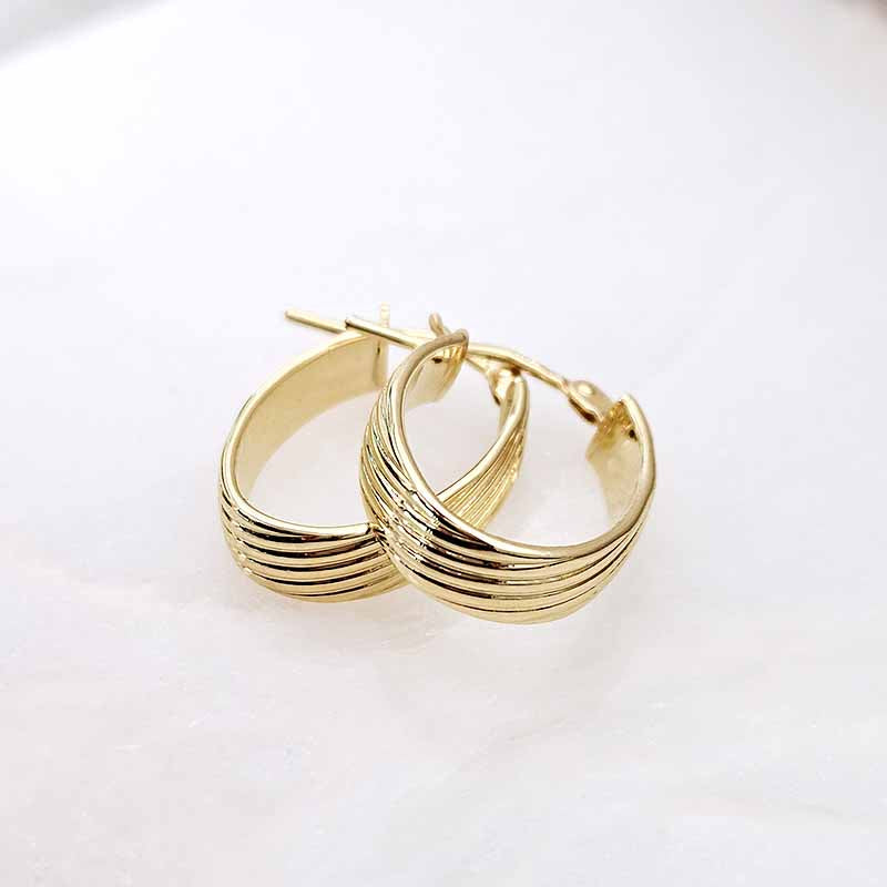 A pair of gold hoop earrings with a multi-row textured design, displayed on a clean white surface.