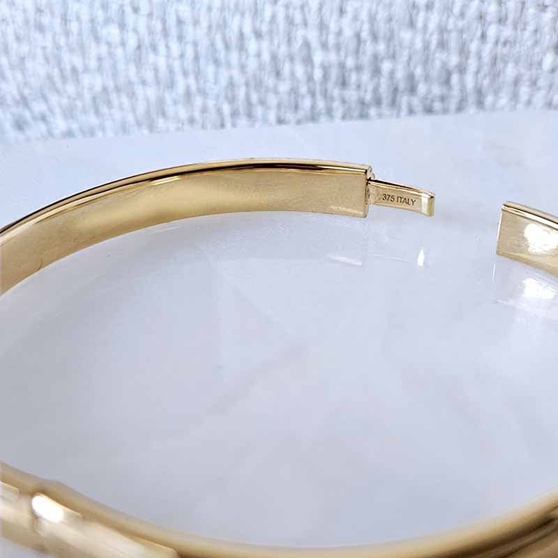 A close-up of a polished gold bangle bracelet with a smooth, curved design, showing a small interior hallmark stamp that reads '375 ITALY'.