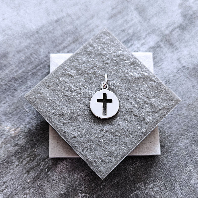 Silver cross pendant on a gray stone surface