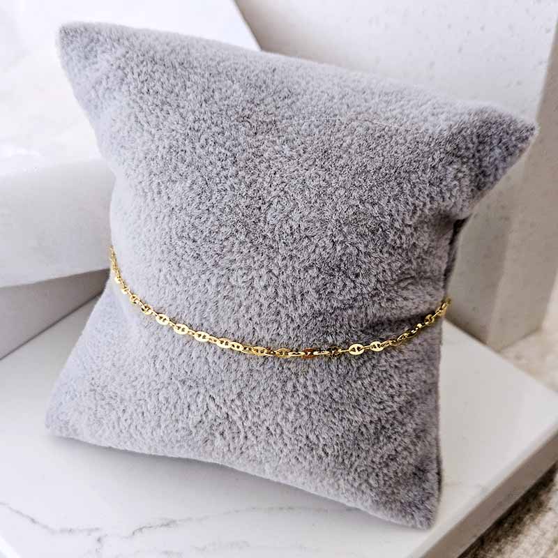 A delicate gold chain bracelet with small smiley face charms, displayed on a textured gray throw pillow.