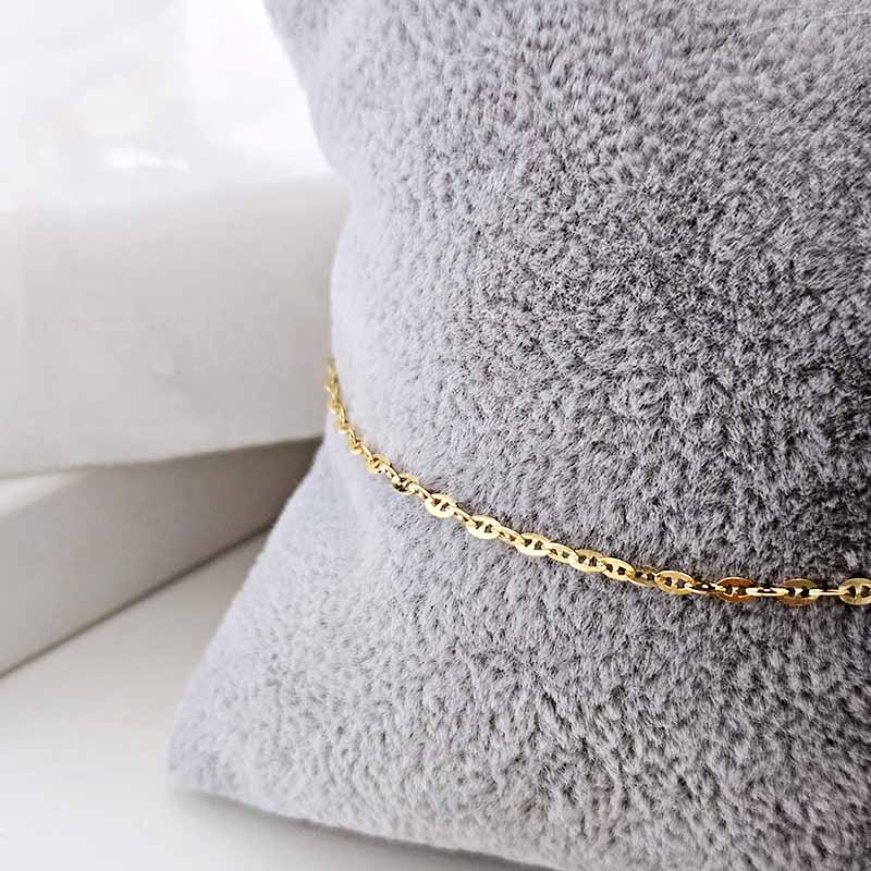 A close-up of a delicate gold chain bracelet draped across a soft, textured gray pillow.