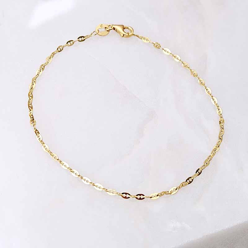 A delicate gold chain bracelet with a twisted link design and a lobster clasp, displayed on a soft white marble surface.