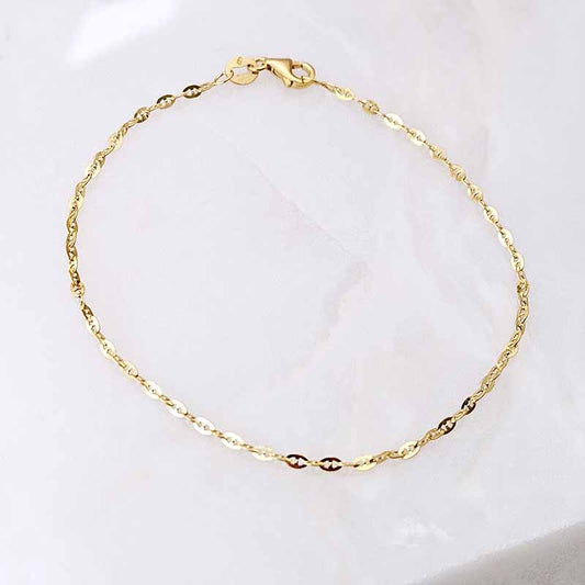 A delicate gold chain bracelet with a twisted link design and a lobster clasp, displayed on a soft white marble surface.