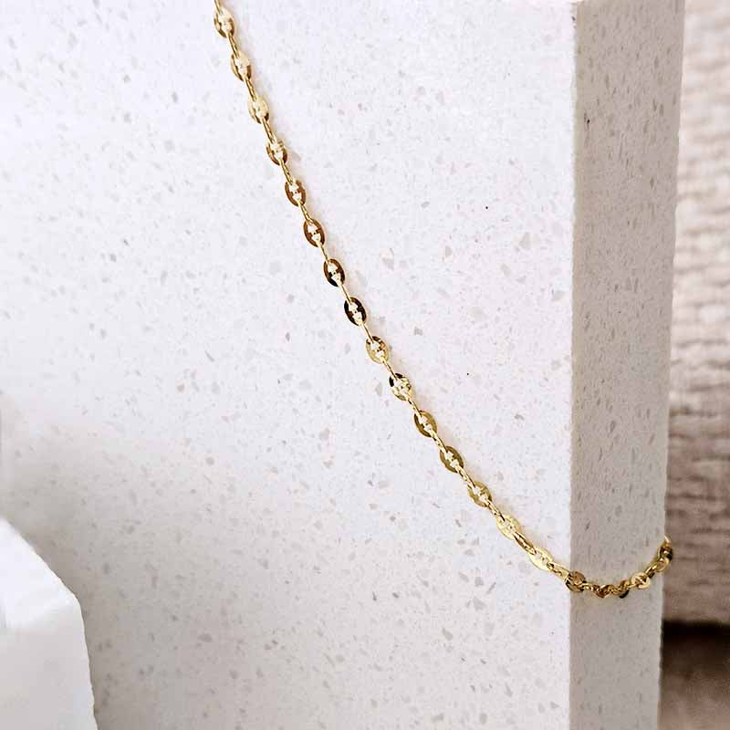 A delicate gold chain necklace draped diagonally across a textured white stone block display.