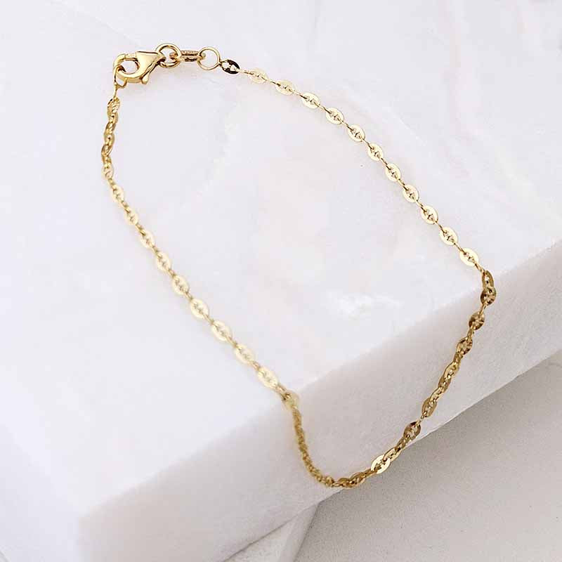 A delicate gold chain bracelet with a lobster clasp, displayed on a white marble block against a white background.