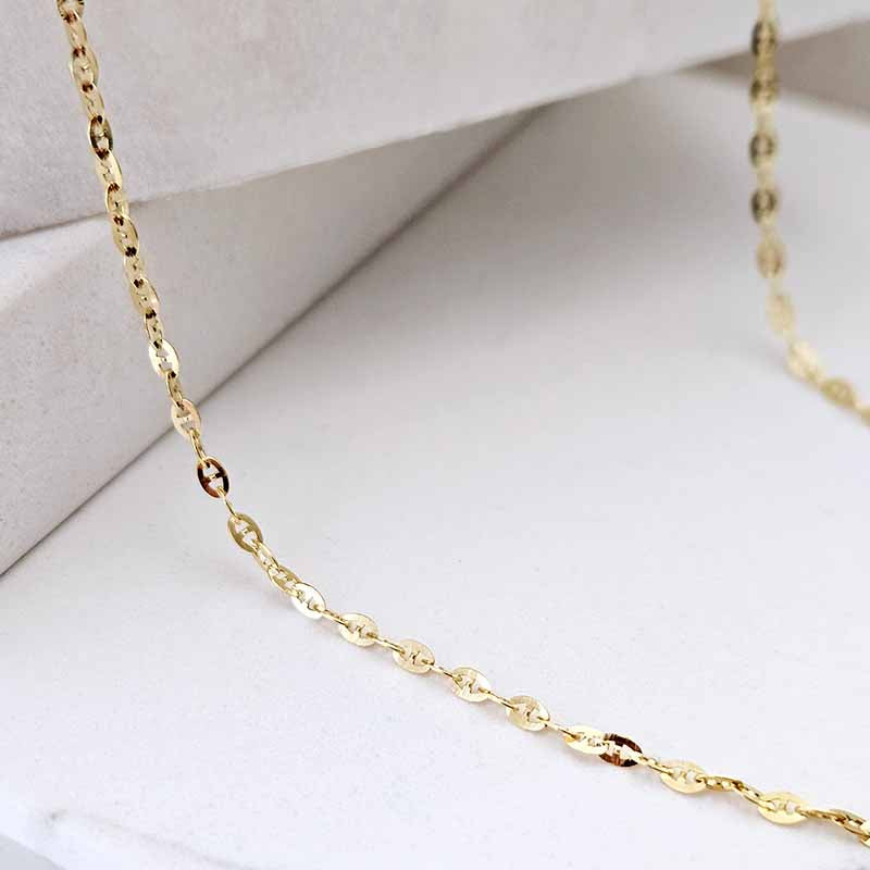 A close-up of a delicate gold chain necklace draped across a white jewelry display box.