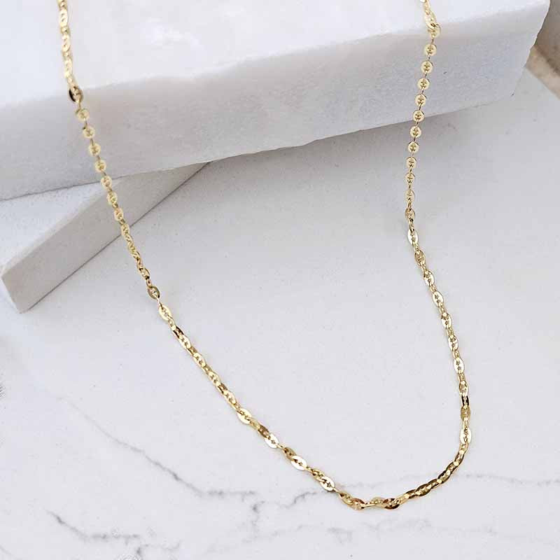 A delicate gold chain necklace draped over a white marble surface with a white marble block in the background.