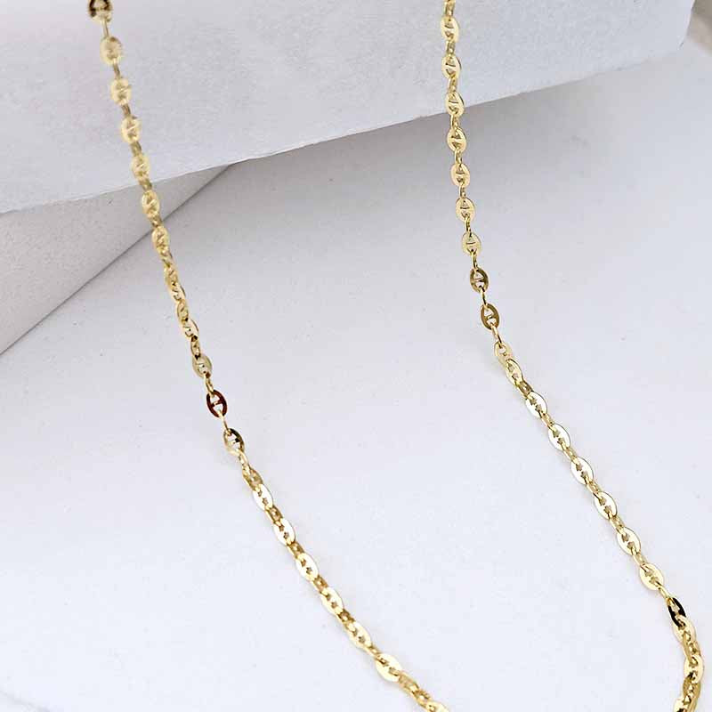 A close-up of a delicate yellow gold chain necklace draped over a white display stand.