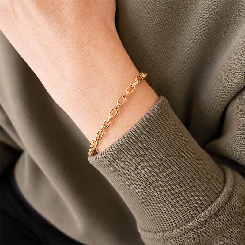 A close-up of a delicate gold chain bracelet worn on a person's wrist, paired with a ribbed olive green sweatshirt.