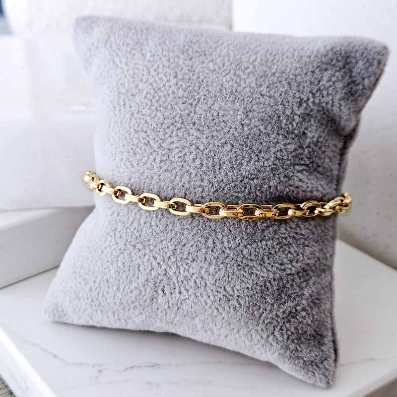 A gold chain belt with a chunky oval link design, displayed on a plush gray throw pillow.