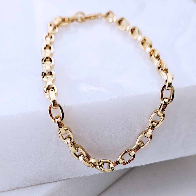 A gold chain link necklace with a polished finish, arranged in a circle on a white textured display block.