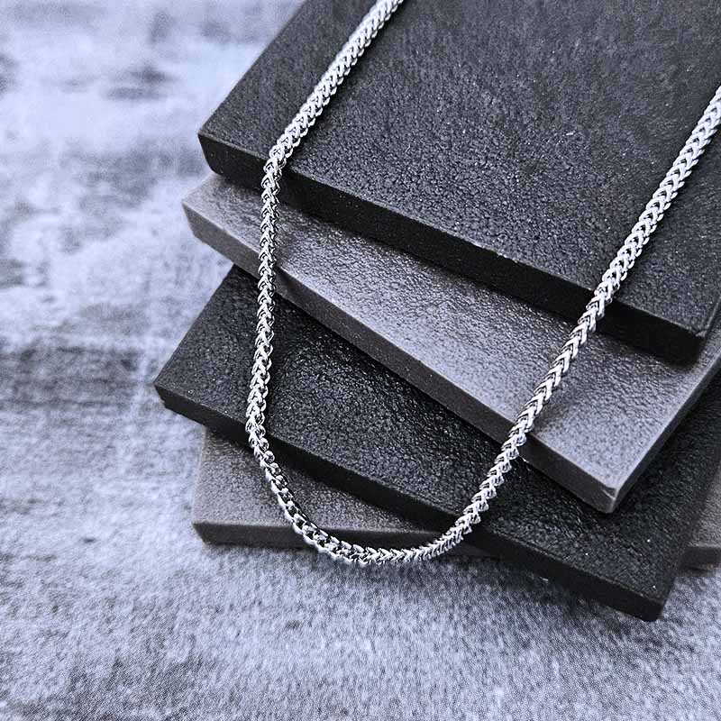 Platinum chain necklace on a stack of black textured blocks with a gray concrete background