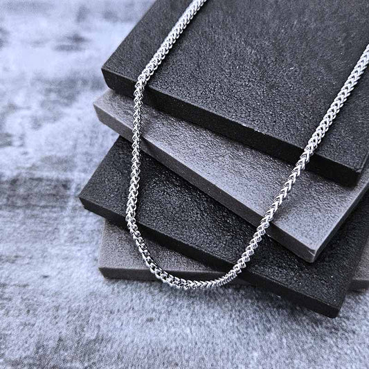 Platinum chain necklace on a stack of black textured blocks with a gray concrete background