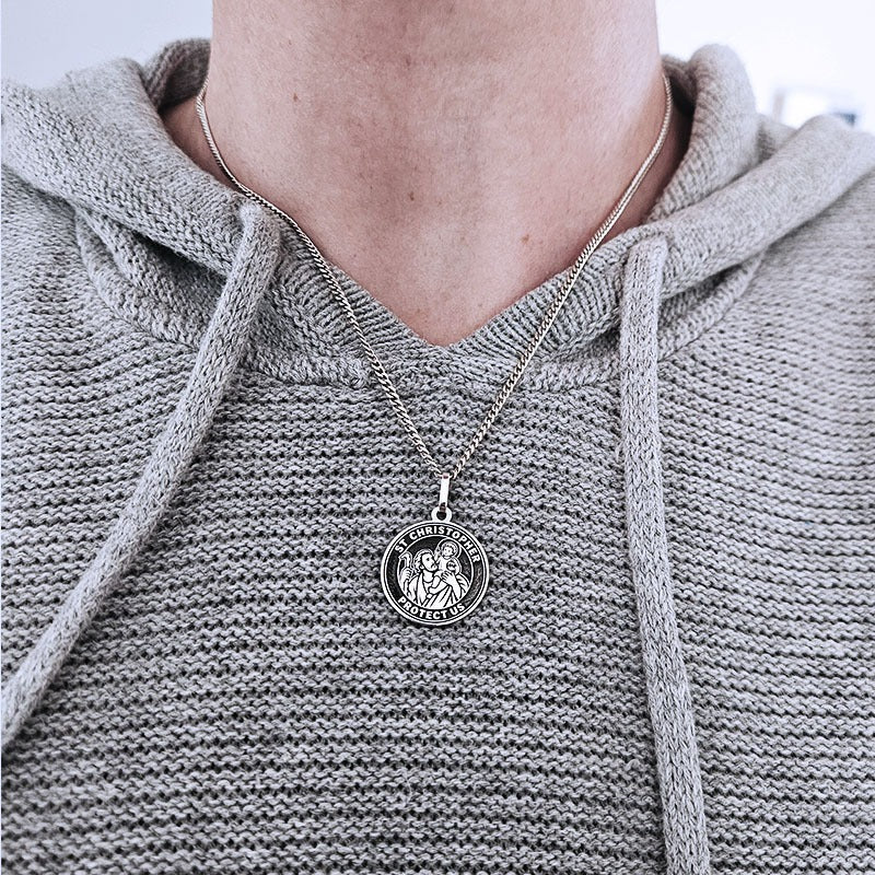 Person wearing a silver necklace with a pendant on a plain background