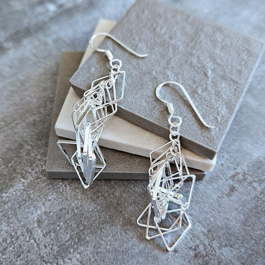 Silver geometric earrings on a textured surface