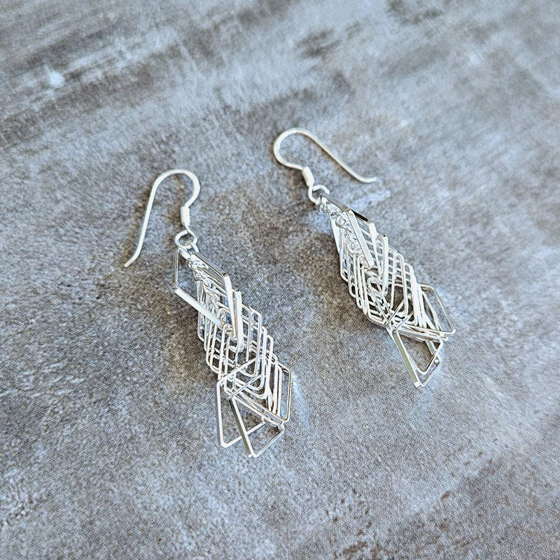 Pair of silver geometric earrings on a textured surface