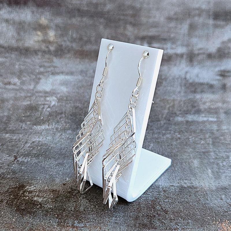 Silver earrings on a white stand against a textured gray background